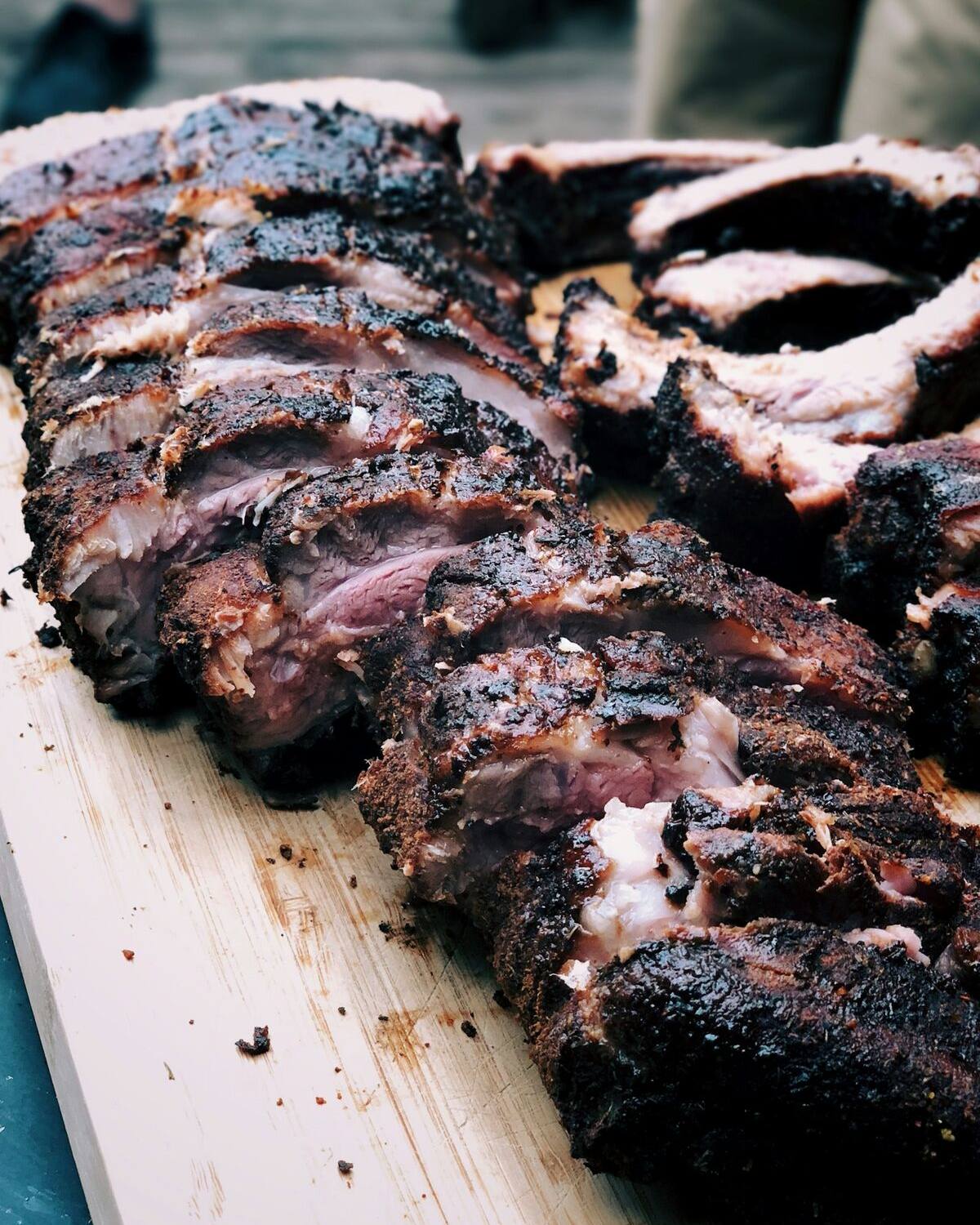 Plate-cut beef ribs resting on a board after a long cook, bark almost black.